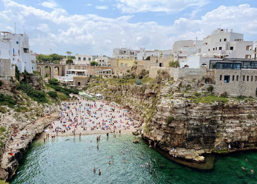 Polignano A Mare Puglia Beach Crowds Turquoise Sea With Cliffs And White Buildings