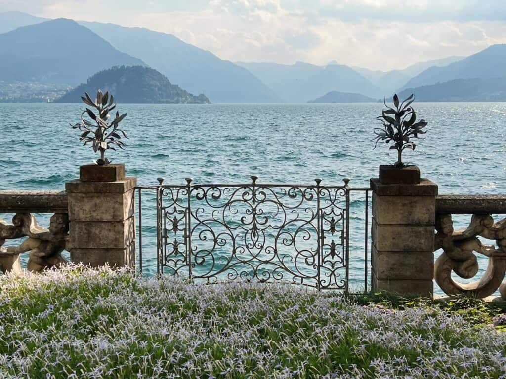 Lake Como View From Villa Monastero Flowers And Wrought Iron Gate Overlooking Lake And Mountains