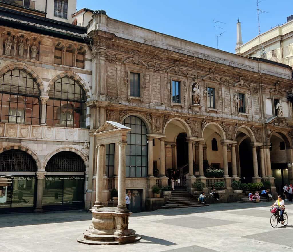 Milan Piazza Mercanti Medieval Square Buildings With Striped Arches Woman Riding Bike People Sitting On Steps